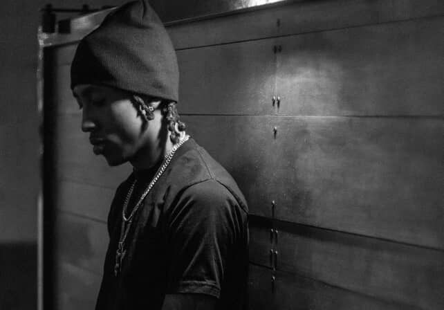 Infamous Moon in deep reflection, leaning against a wall in black and white tones.